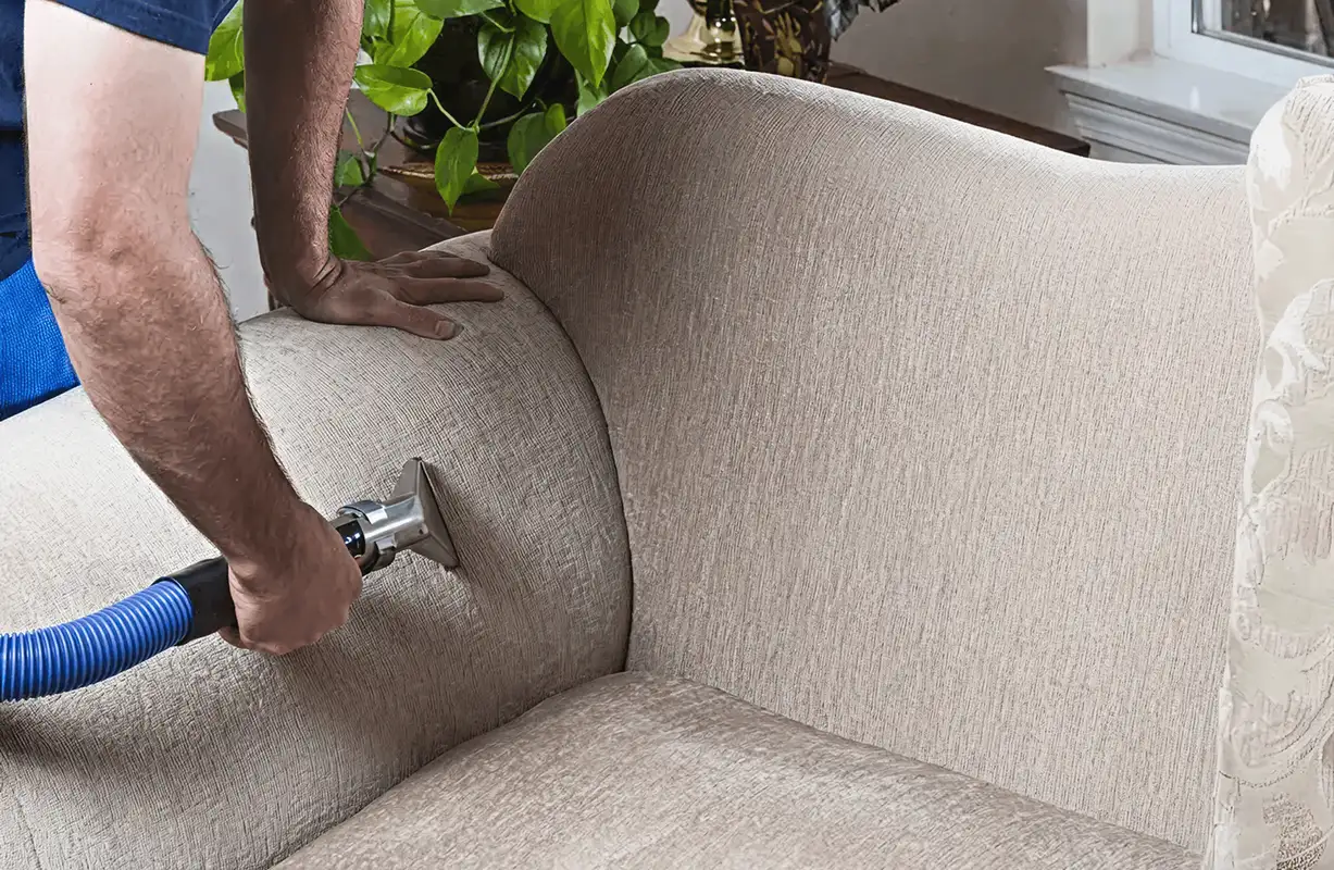 Professional upholstery cleaner deep-cleaning a fabric sofa with a handheld extraction tool and hose, Richmond, VA.